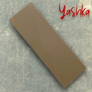 May include: An olive-brown rectangular fabric piece with a textured surface. The word "Yashka" is written in red cursive script in the upper right corner. The fabric has a subtle woven pattern.