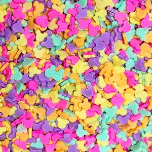 May include: A large assortment of colorful sprinkles shaped like Mickey Mouse heads. The sprinkles are in shades of yellow, orange, pink, purple, and green.