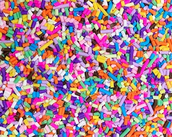 May include: A close-up of a variety of colorful sprinkles. The sprinkles are in a variety of shapes and sizes, including long, thin sprinkles, round sprinkles, and star-shaped sprinkles. The sprinkles are a mix of pink, purple, blue, green, yellow, orange, and brown.