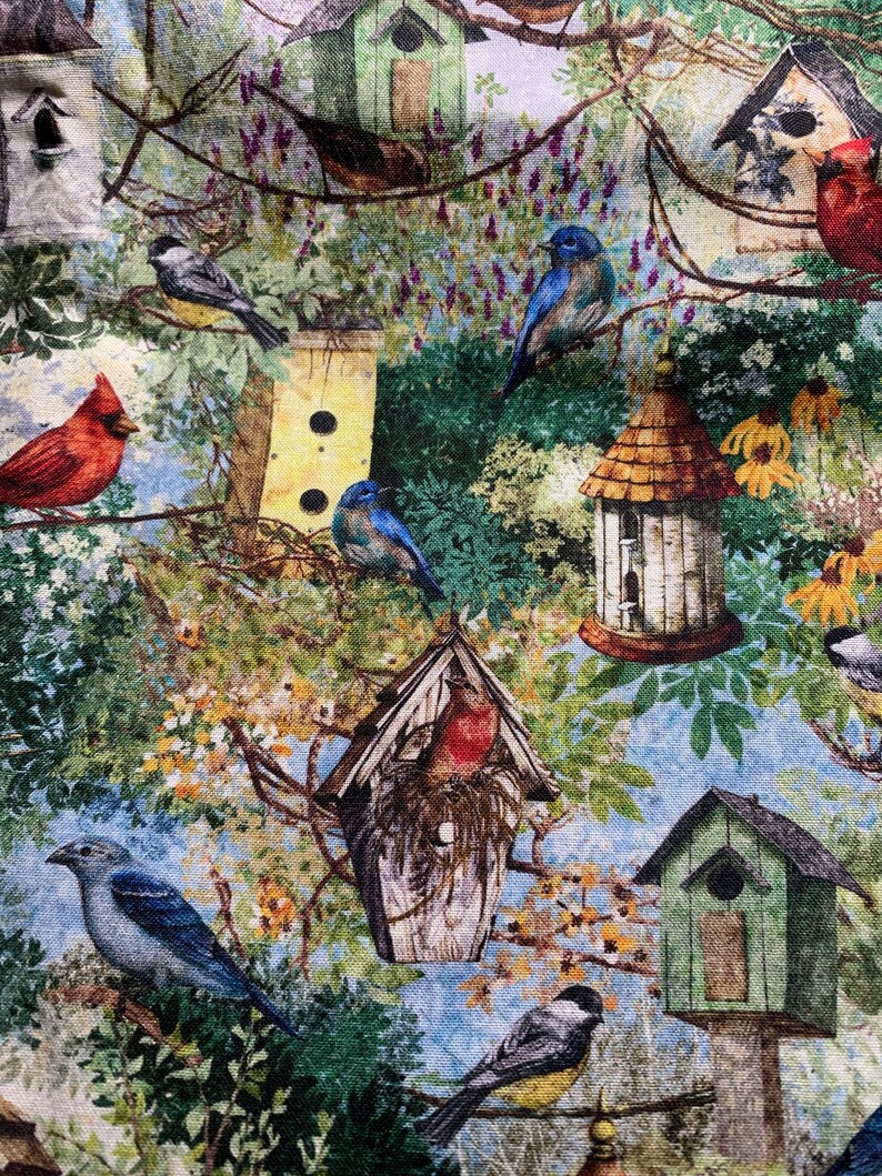 Puede incluir: Una tela colorida con un patr&oacute;n repetitivo de casas para p&aacute;jaros, p&aacute;jaros y flores. Las casas para p&aacute;jaros est&aacute;n pintadas en tonos de verde, marr&oacute;n y amarillo. Los p&aacute;jaros son azules, rojos y marrones. Las flores son amarillas, rosas y moradas.