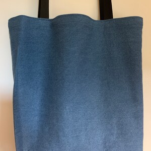 May include: A blue denim tote bag with black straps. The bag is made of a sturdy fabric and has a spacious interior.
