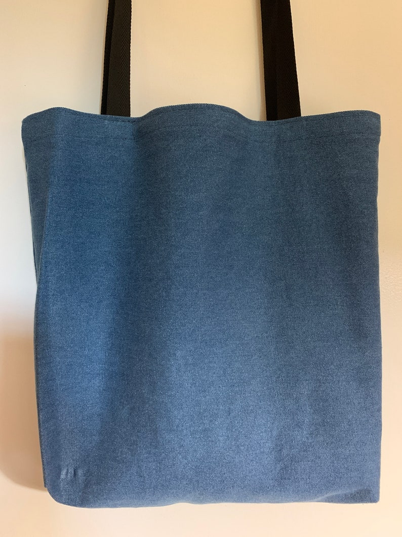 May include: A blue denim tote bag with black straps. The bag is made of a sturdy fabric and has a spacious interior.