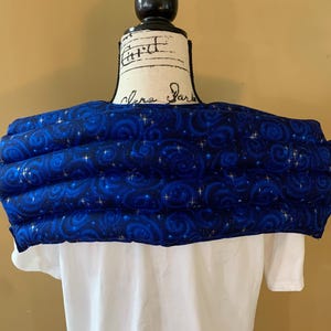 May include: A blue and gold neck wrap with a swirling pattern and stars. The wrap is made of soft fabric and is designed to provide comfort and warmth.