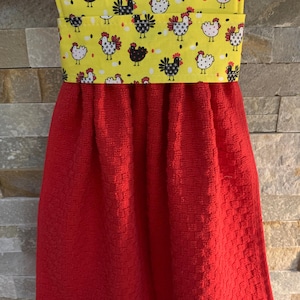 May include: Red kitchen towel with a yellow and white fabric band featuring a repeating pattern of black and white chickens. The band is folded over at the top to create a hanging loop.