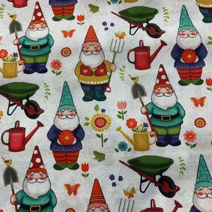 Puede incluir: Una tela blanca con un patr&oacute;n repetido de gnomos, flores, mariposas, carretillas, palas y regaderas. Los gnomos llevan sombreros y ropa de diferentes colores. Las flores son rojas, amarillas y rosas. Las mariposas son naranjas y blancas. Las carretillas son verdes. Las palas son marrones. Las regaderas son rojas y amarillas.