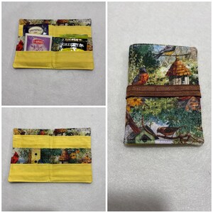 May include: A handmade tea wallet with a yellow exterior and a birdhouse and bird pattern. The wallet is open, revealing tea bags. The wallet is closed with a brown elastic band.