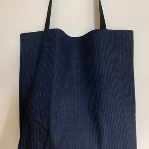 May include: A dark blue tote bag with black straps. The bag is made of a striped fabric.
