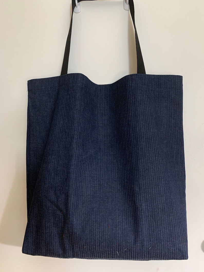 May include: A dark blue tote bag with black straps. The bag is made of a striped fabric.