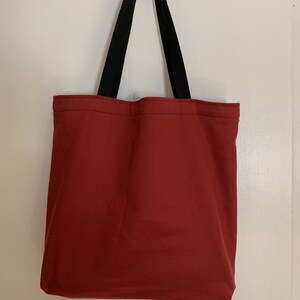 May include: A red tote bag with black straps. The bag is made of a sturdy canvas material.