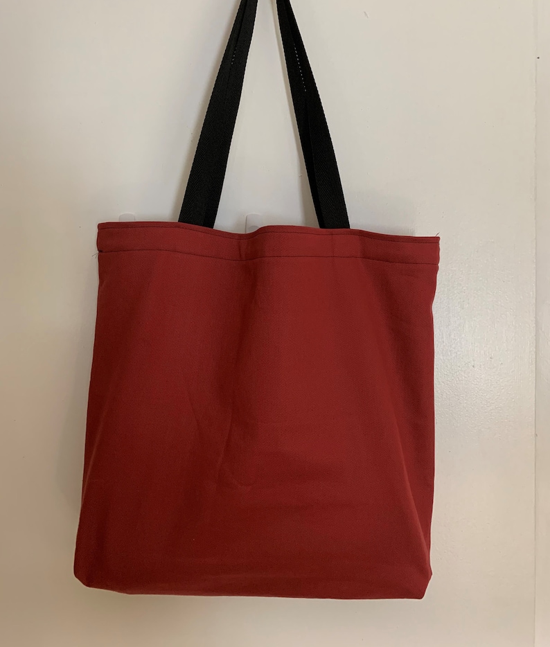 May include: A red tote bag with black straps. The bag is made of a sturdy canvas material.