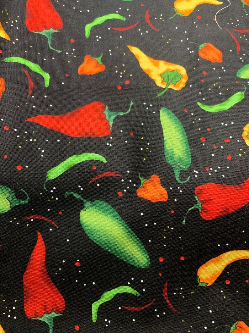 May include: A black fabric featuring a repeating pattern of various chili peppers in shades of red, orange, yellow, and green. The design is accented with small white and red dots scattered across the dark background, creating a vibrant culinary print.
