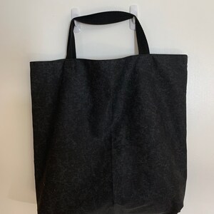 May include: A black canvas tote bag with black fabric handles. The bag is hanging on a white wall.