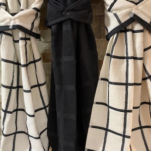 May include: Three kitchen towels hanging on a rack. Two towels are white with black grid patterns, and one towel is black with a grid pattern.