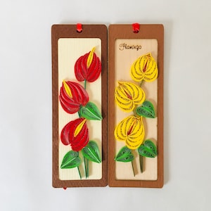 Könnte beinhalten: Zwei Holzbuchzeichen mit roten und gelben Papierblumen. Das Buchzeichen rechts trägt den Schriftzug "Flamingo".