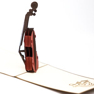 May include: A red and brown paper pop-up card featuring a cello. The card is open and the cello is standing upright.