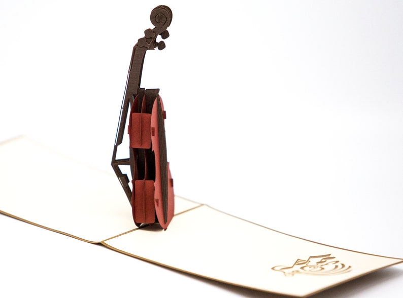 May include: A red and brown paper pop-up card featuring a cello. The card is open and the cello is standing upright.
