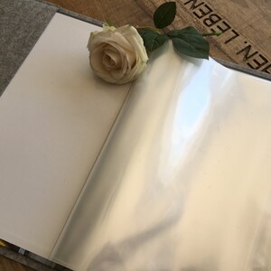 May include: A gray felt-covered book with a clear plastic page protector. A white rose with green leaves is placed on the book.