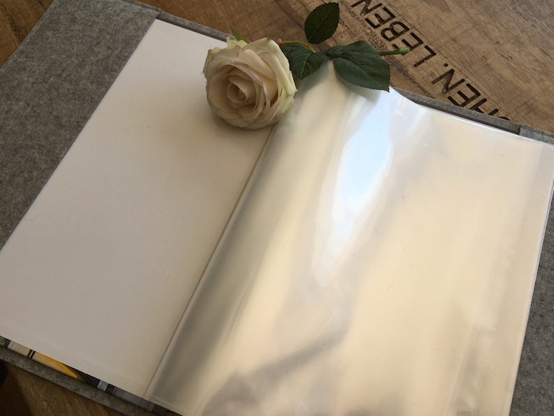 May include: A gray felt-covered book with a clear plastic page protector. A white rose with green leaves is placed on the book.