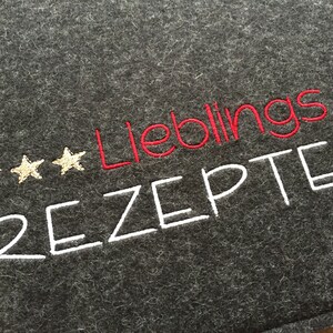 May include: Dark gray felt recipe holder with embroidered text. The word "Lieblings" is in red, and "Rezepte" is in white. Three gold stars are embroidered above the word "Lieblings".