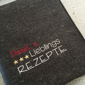 May include: Dark gray felt recipe book cover with embroidered text. The text reads "Daniel's Lieblings REZEPTE" in white and red thread, with three gold stars. A handmade item.