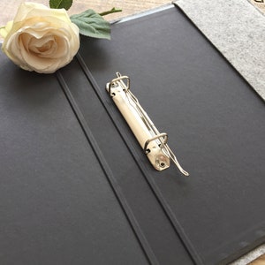 May include: A black binder with a grey felt cover and a silver metal ring binder mechanism.