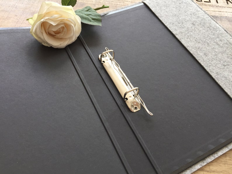 May include: A black binder with a grey felt cover and a silver metal ring binder mechanism.