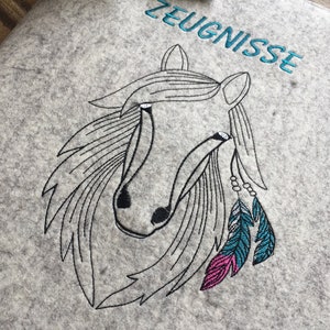 May include: Embroidered design of a horse's head with feathers and beads on a gray felt background. The text "ZEUGNISSE" is embroidered in blue above the horse.