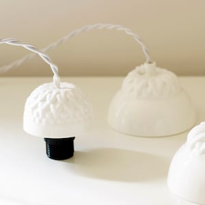 May include: Three white ceramic pendant light fixtures with a textured surface and black electrical cords.