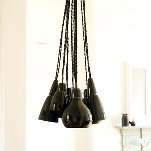 May include: A black pendant light fixture with multiple black ceramic shades hanging from black braided cords.