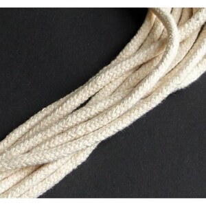 May include: Close-up of several strands of off-white, braided rope against a black background. The rope appears to be made of a natural fiber, with a slightly textured surface. The strands are arranged diagonally across the frame.