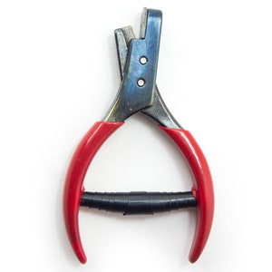 Puede incluir: Una herramienta de metal con mangos rojos y un agarre negro. La cabeza de la herramienta es azul y plateada, asegurada con dos pequeños remaches. Los mangos curvos son rojos, y el agarre es negro y envuelto.