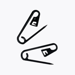 Puede incluir: Dos imperdibles de color negro mate con un diseño de espiral clásico en la base y una punta afilada. Cada imperdible cuenta con un mecanismo de cierre seguro con un broche triangular plano que mantiene la punta fija cuando está cerrado.