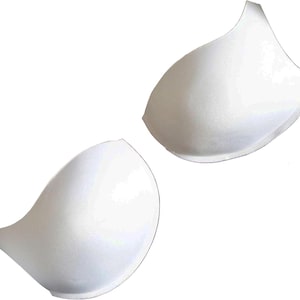 May include: Two white bra cup inserts, each with a curved, petal-like shape. The inserts are made of a smooth, solid material and are designed to provide shape and support. The background is plain white.