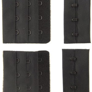 Op de afbeelding: Vier zwarte bh-verlengstukken met haak- en oogsluitingen. Twee verlengstukken hebben drie rijen haken en ogen, en twee verlengstukken hebben twee rijen haken en ogen.