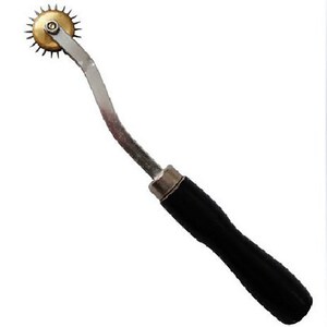 May include: A silver and brass sewing tool with a black handle. The tool has a circular wheel with sharp points and a curved handle.