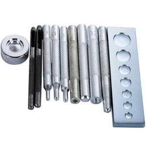 May include: A set of metal tools for leathercraft. The set includes various punches, a metal plate with circular holes, and a small, round metal piece. The tools have silver handles and black tips.