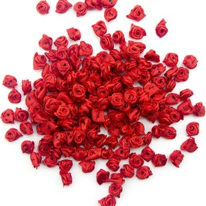 May include: A scattering of small, bright red satin ribbon roses on a white background. Each rose is meticulously crafted, displaying delicate petals and a compact shape. These decorative embellishments are suitable for craft projects.
