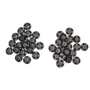 May include: Two piles of black snap fasteners with silver centers are displayed against a white background. The fasteners have a circular design with small holes around the edge. These are commonly used in sewing and crafting projects.