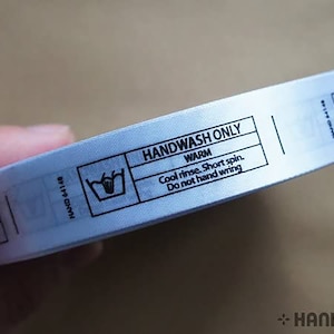 Op stof bedrukte waslabels: ALLEEN MET DE HAND WAS, 20 x 68 mm, rol van 1000, set van 2