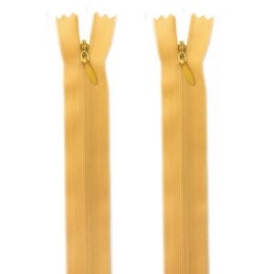 May include: Two beige zipper pulls with gold metal sliders. The zippers are closed and ready to be sewn into a garment.