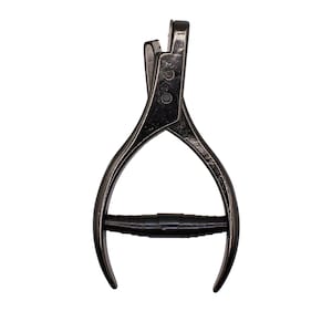 May include: A dark metallic hole punch tool featuring a spring-loaded mechanism and a central black cylindrical grip. The tool has two curved handles that meet at a pivot point, with a small punch head at the top designed for creating circular holes.