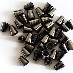 Op de afbeelding: Een verzameling kleine, conische metalen koordeinden met een gepolijste gunmetal afwerking. Elk onderdeel heeft een holle binnenkant en een taps toelopende vorm, ontworpen voor het vastzetten van de uiteinden van koorden op diverse textielartikelen.