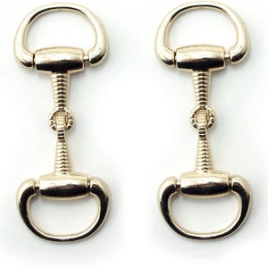 May include: Two gold-toned metal snaphook clasps with a decorative twisted design. The clasps are open and ready to be attached to a project.