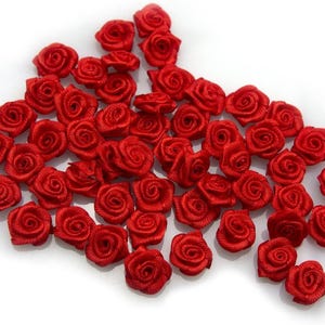 Peut inclure: Un ensemble de petites roses en satin rouge vif. Chaque fleur est soigneusement enroulée, révélant un centre en spirale et des pétales délicats. Les roses sont dispersées, parfaites pour les travaux manuels et la décoration.