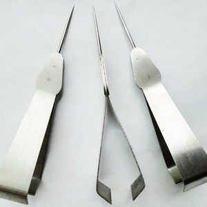 Könnte beinhalten: Drei silberne Metallwerkzeuge mit spitzen Spitzen und Griffen. Die Werkzeuge sind zum Entfernen von Samen aus Obst und Gemüse gedacht.