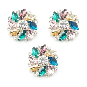 May include: Three silver-toned, multi-coloured rhinestone embellishments. Each embellishment features a circular design with a central clear rhinestone surrounded by smaller rhinestones in shades of pink, green, blue, and gold.