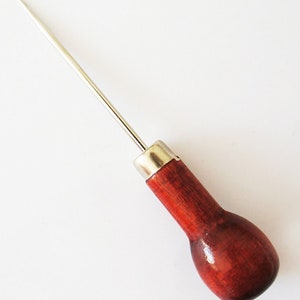 Könnte beinhalten: Nahaufnahme eines Leder-Stechbeitels mit einem Holzgriff. Der Stechbeitel hat eine scharfe, spitze Spitze und eine Metallhülse.