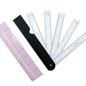 May include: A clear rectangular ruler with a pink grid pattern and a set of white folding architect scales attached to a black handle. The white scales feature various numerical markings and ratios, fanned out from a single metal pivot point.