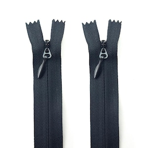 May include: Two black zippers with a closed design are displayed against a white background. Each zipper has a black pull tab and a silver-colored metal slider. The zipper teeth are visible at the top, and the fabric is a dark, solid color.