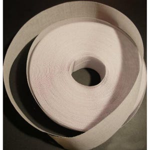 Puede incluir: Un rollo de cinta blanca texturizada, enrollada firmemente con un núcleo visible. La cinta es de un color claro y neutro, con los bordes ligeramente deshilachados. La imagen es un primer plano, destacando la textura y la forma de la cinta.